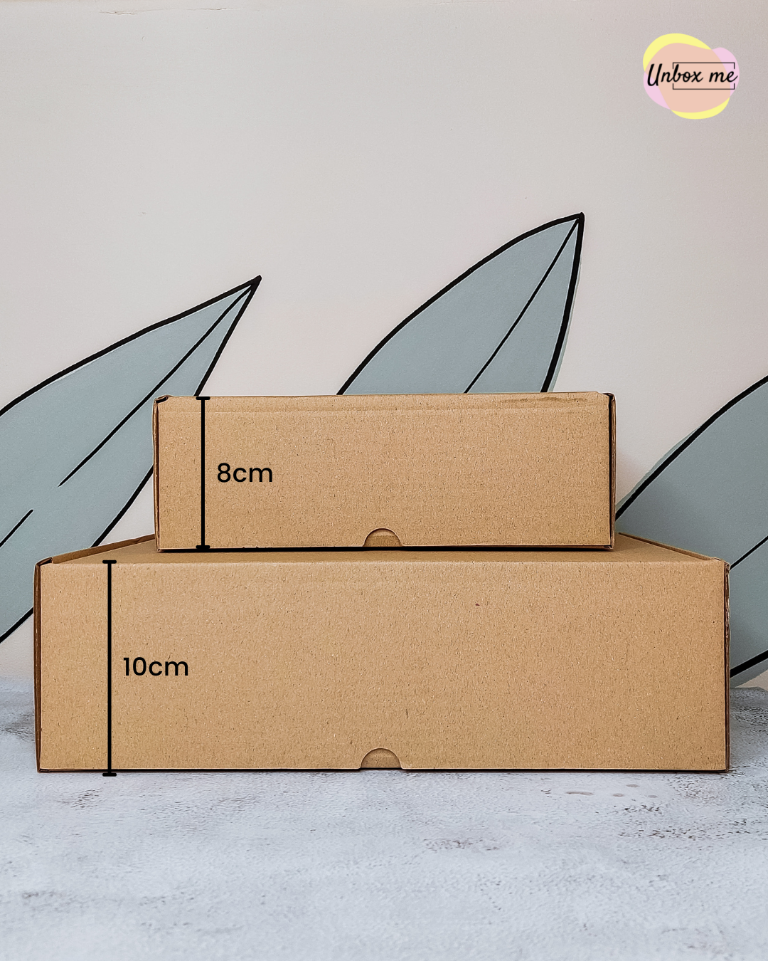 Duas caixas de cartão castanho empilhadas com fundo decorativo e logo Unbox me