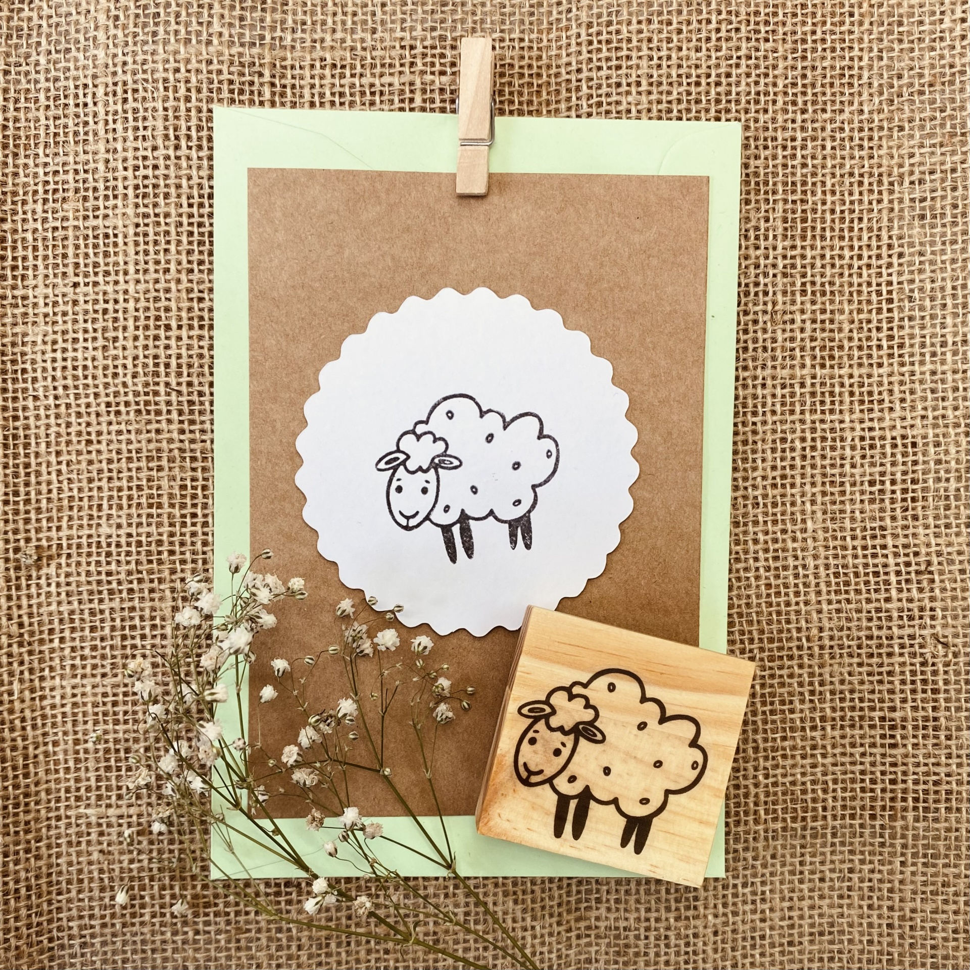 Carimbo de madeira com desenho de carneiro e papel com impressão do carimbo sobre fundo de juta