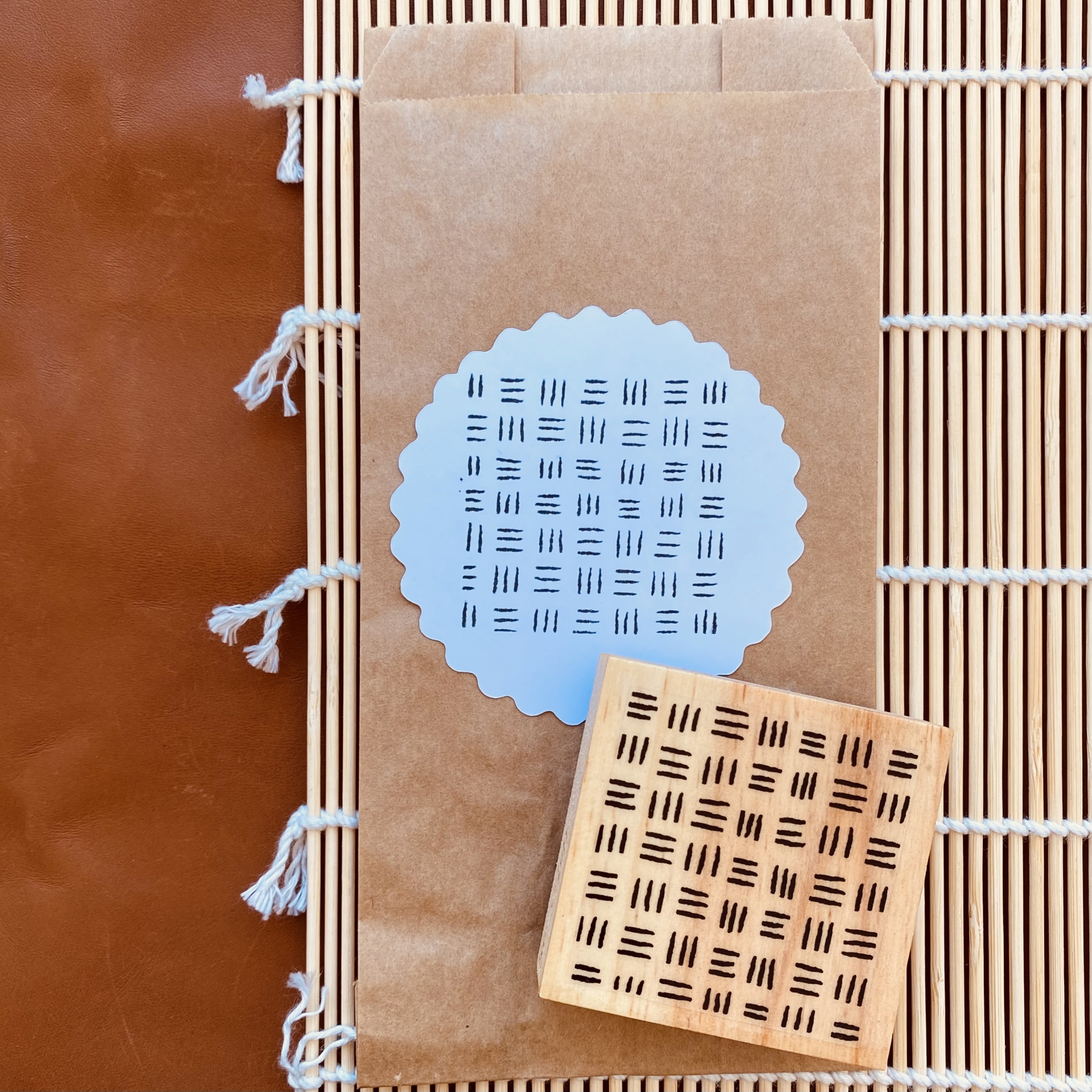 Embalagem de papel castanho com etiqueta branca e objeto quadrado de madeira clara com padrão de linhas pretas