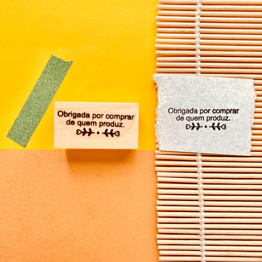 Carimbo de borracha com texto em português e a impressão do carimbo em papel cinzento sobre bambu