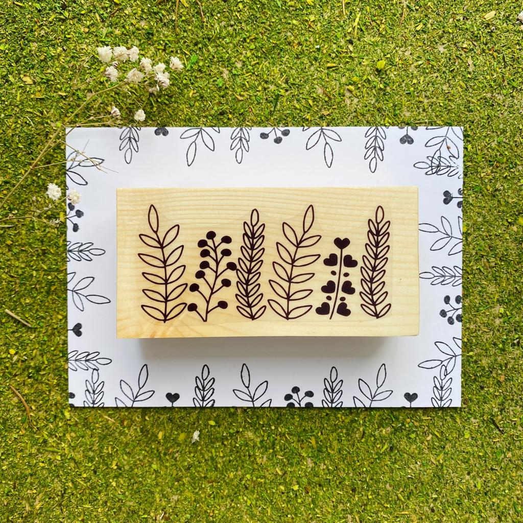 Carimbo de madeira com desenho de plantas sobre papel com padrão preto e branco sobre relva verde