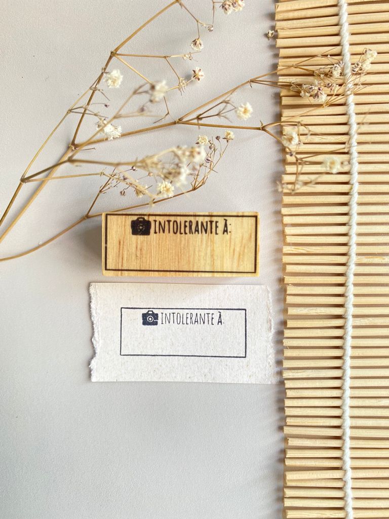 Dois carimbos com texto Intolerante à junto a flores secas e tapete de madeira