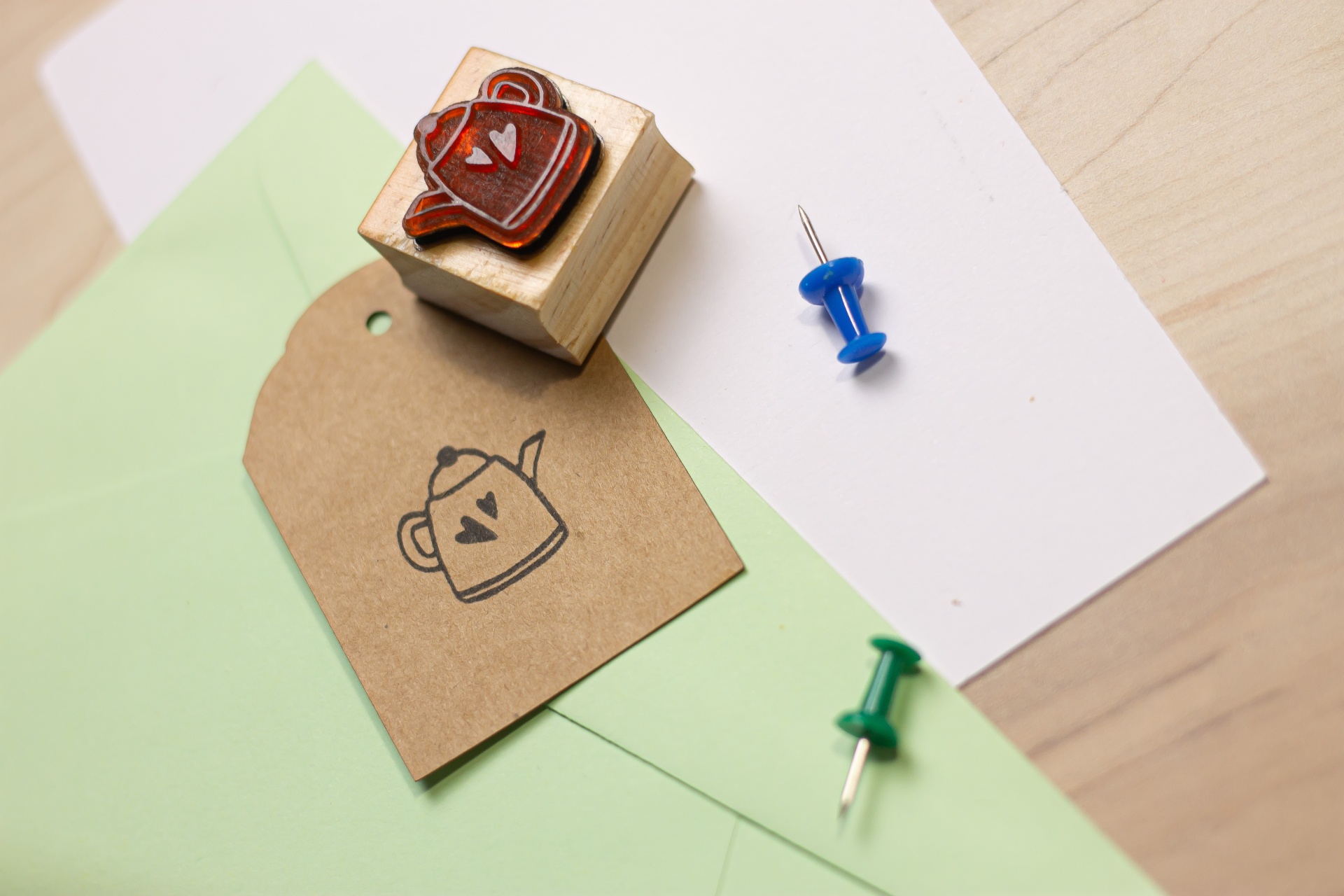 Carimbo com desenho de bule e coração sobre papel castanho colocado em envelopes com alfinetes coloridos