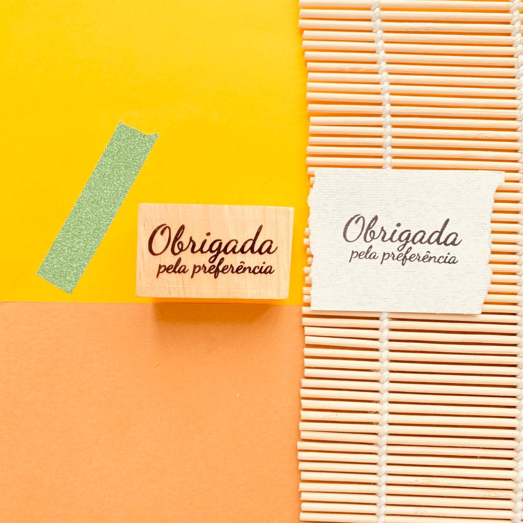Carimbo e impressão 'Obrigada pela preferência' em papel com fundo colorido e fita decorativa