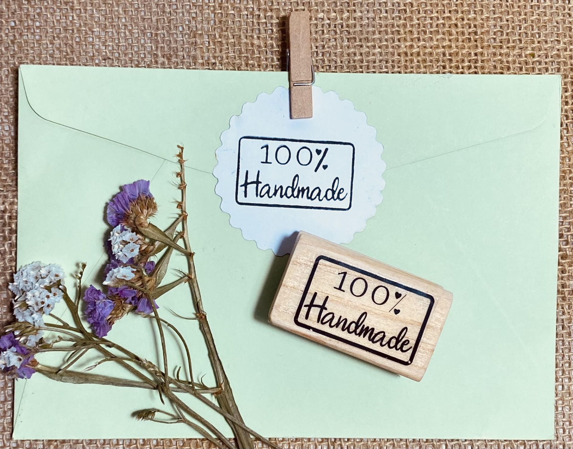 Envelope verde-claro com flores secas e selo com texto '100% Handmade'