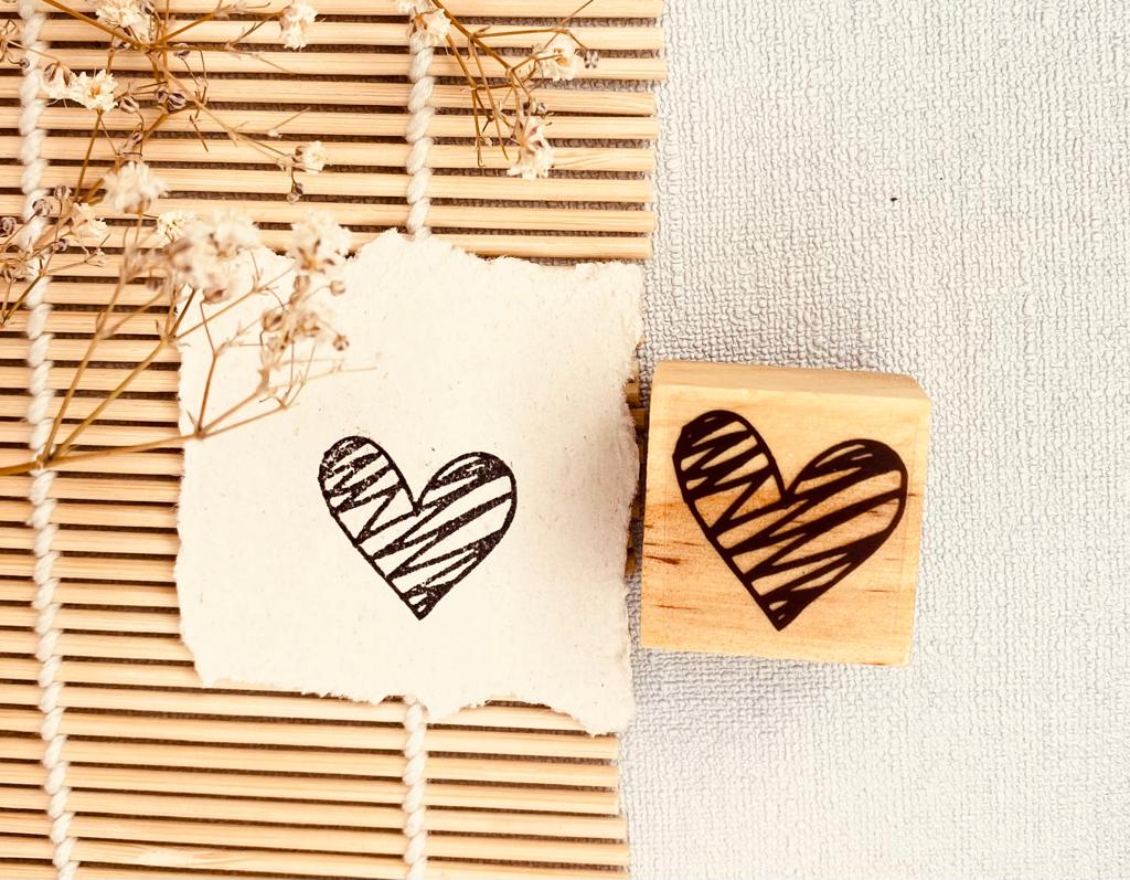 Carimbo de madeira com coração riscado ao lado de papel impresso com o mesmo desenho