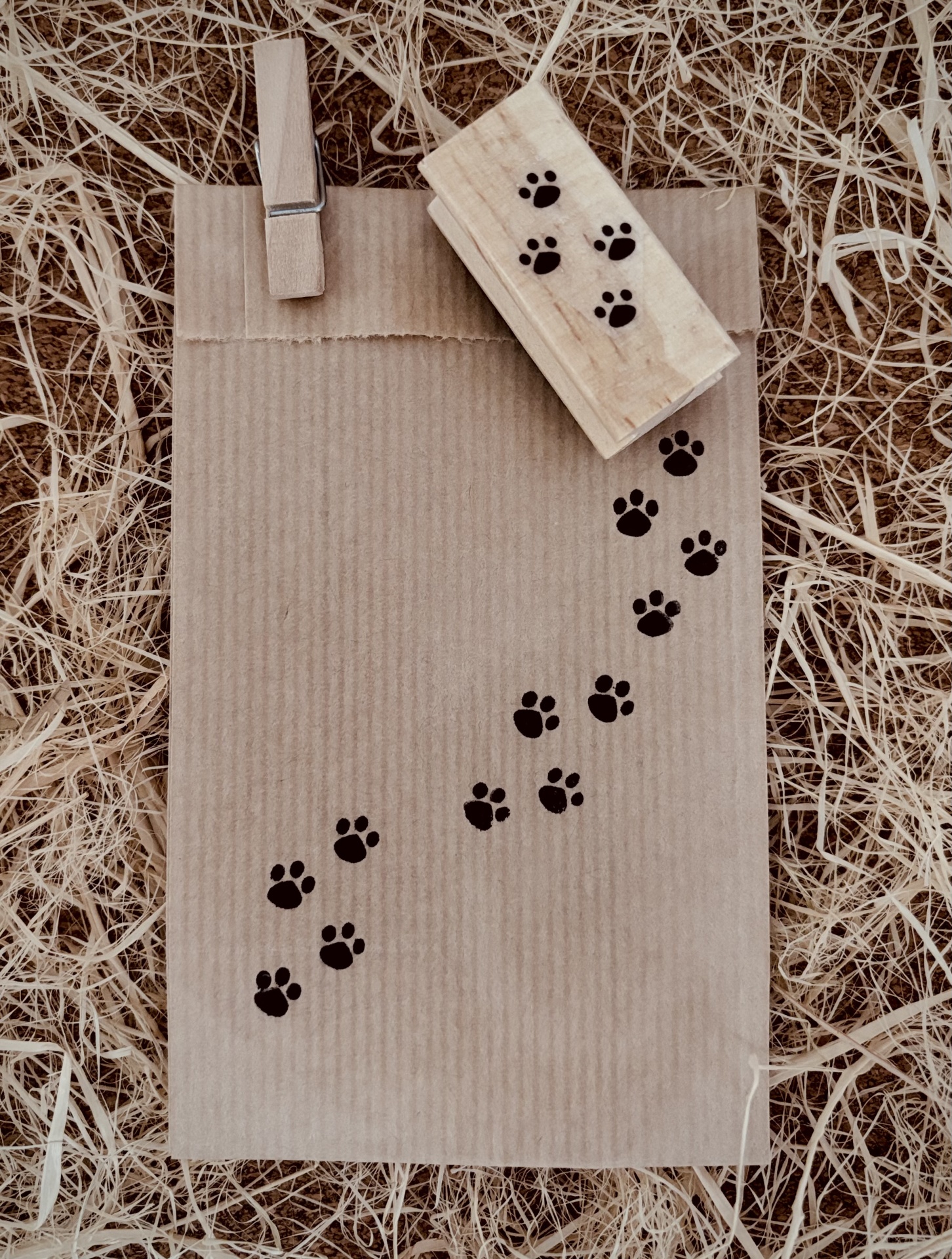 Saco de papel castanho com pegadas pretas e carimbo de madeira sobre palha