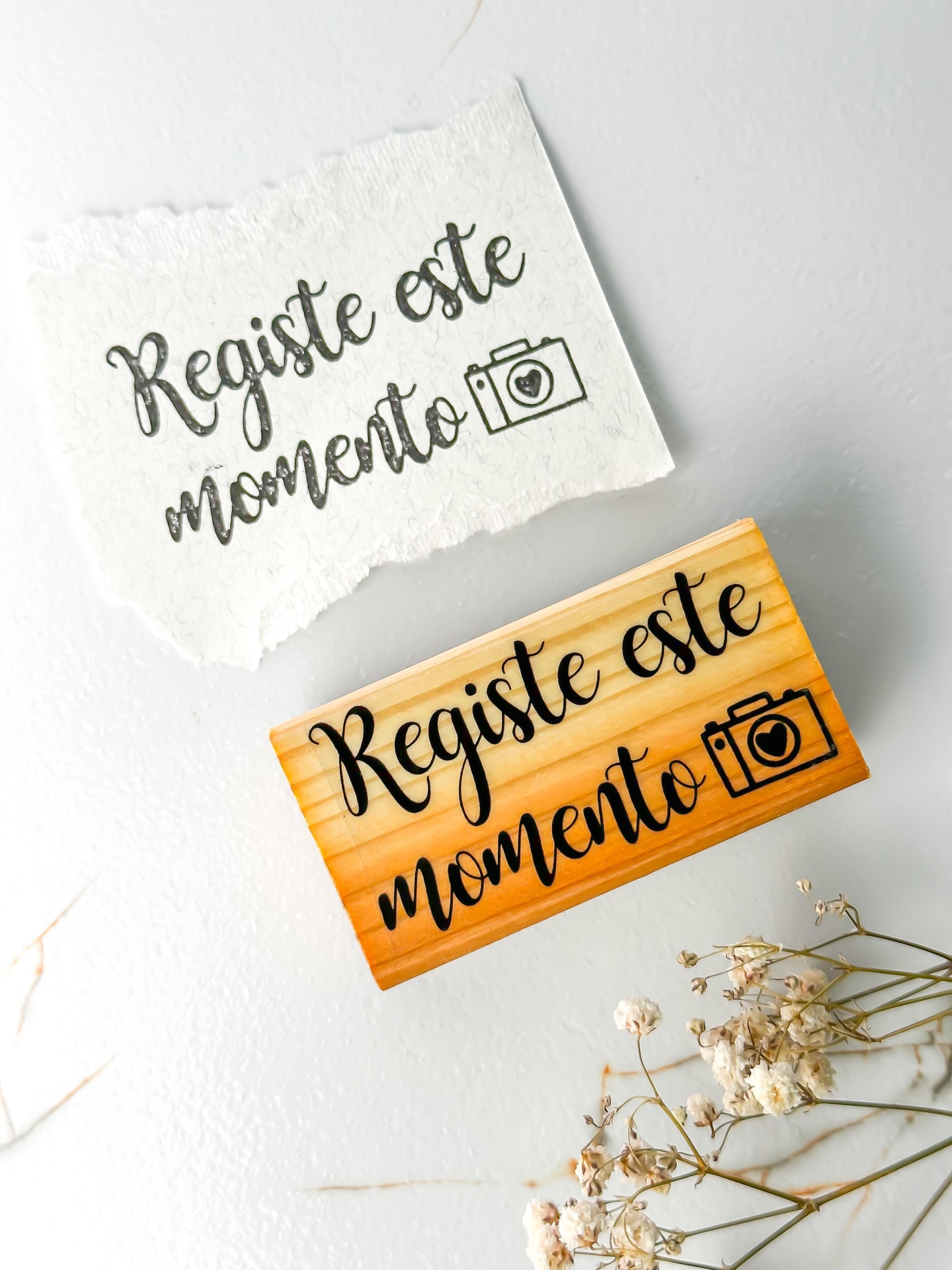 Carimbo de madeira com texto e ícone, papel branco carimbado e flores secas