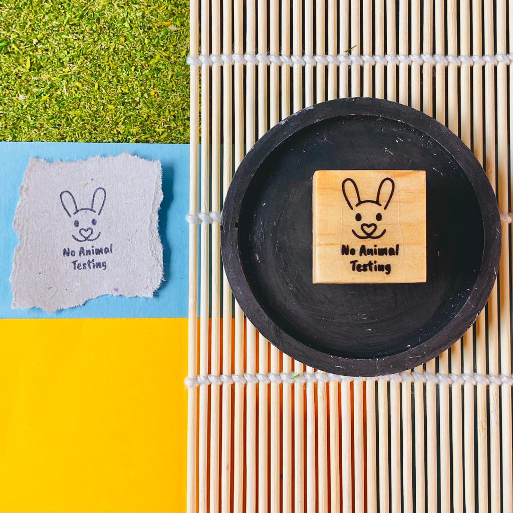 Selo de madeira com desenho de coelho e texto No Animal Testing sobre prato preto e esteira de bambu