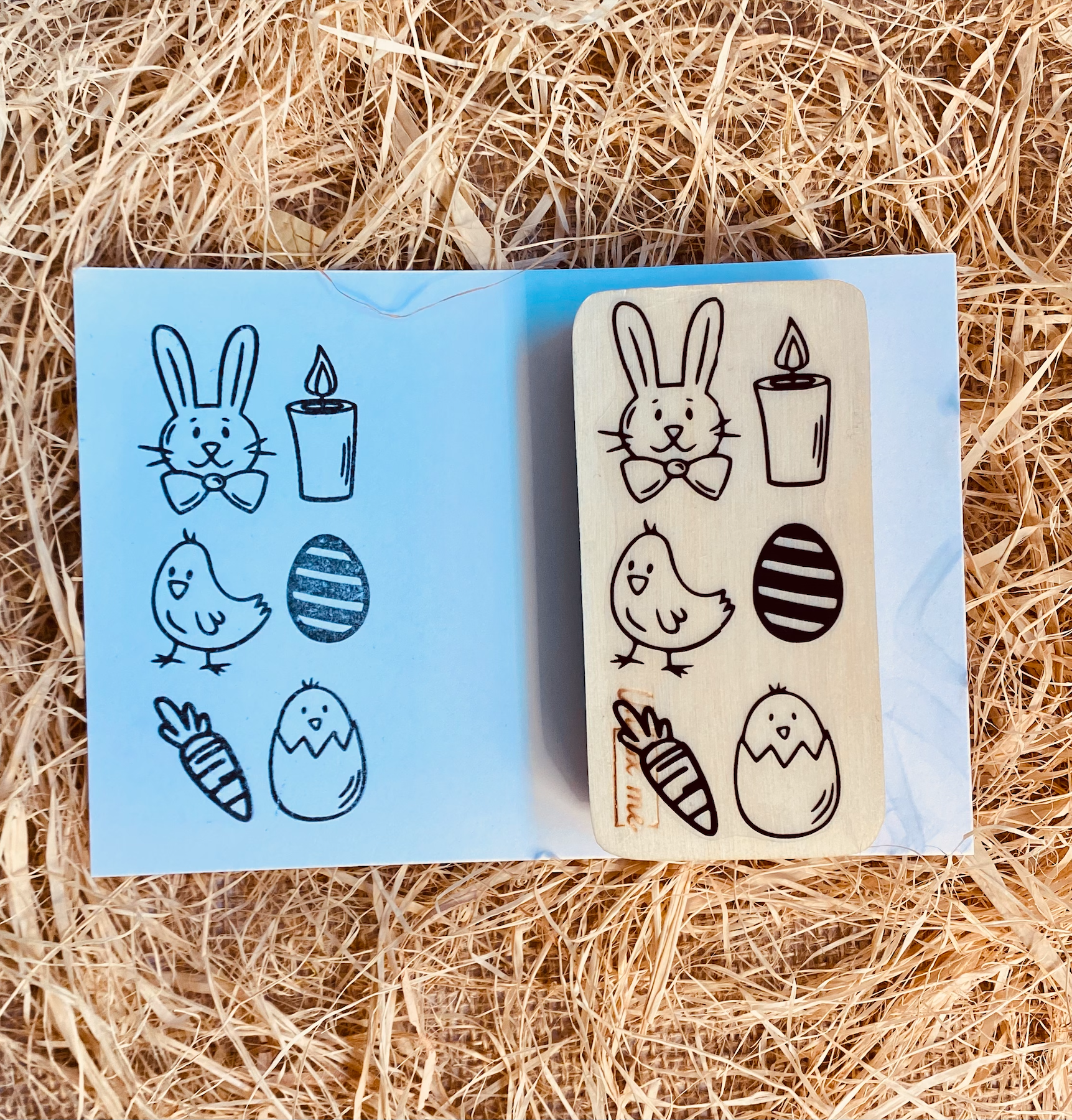 Carimbo de madeira com desenhos de Páscoa sobre cartão azul e palha