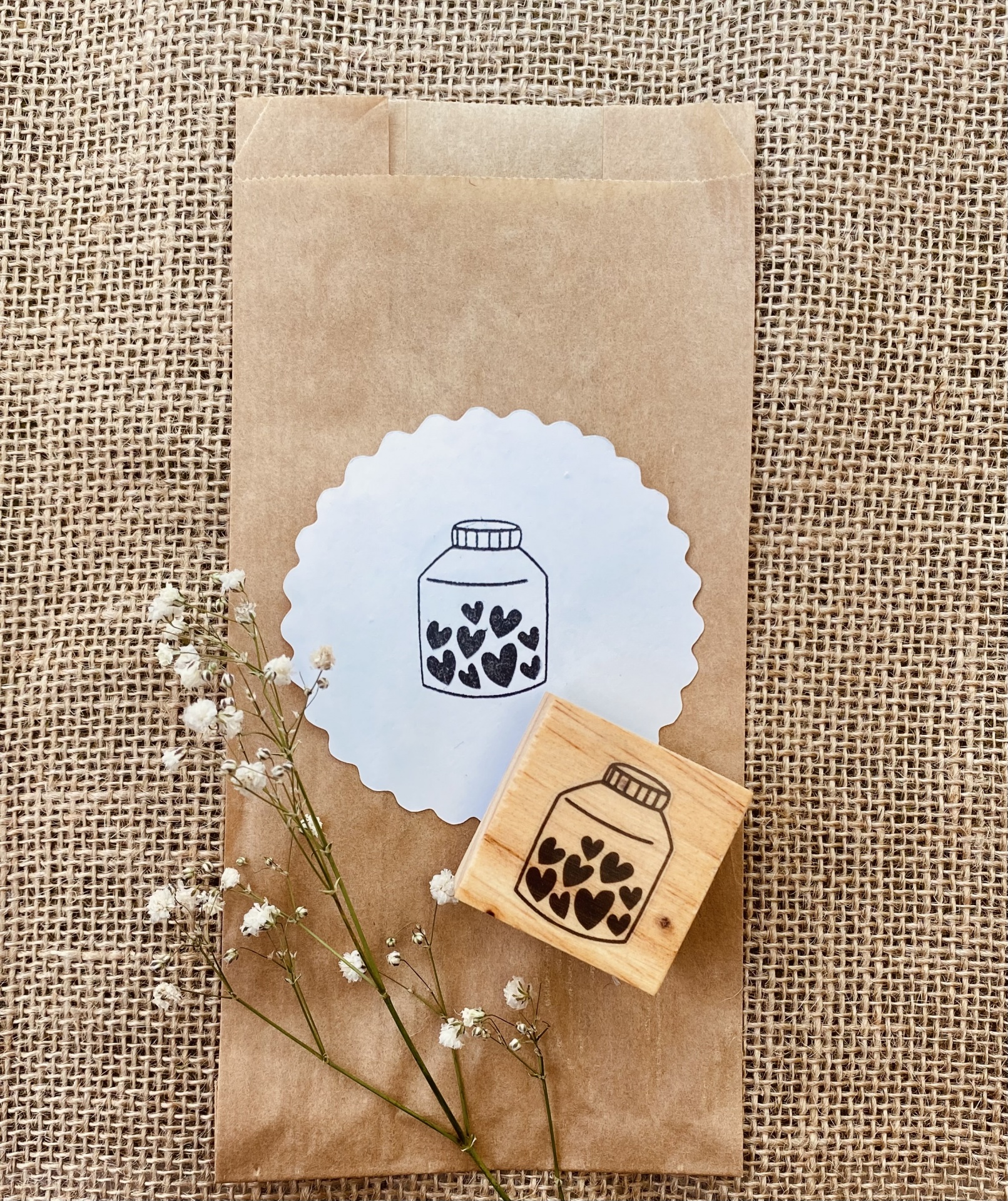 Selo decorativo, saco de papel, carimbo de madeira e flores secas sobre tecido rústico.