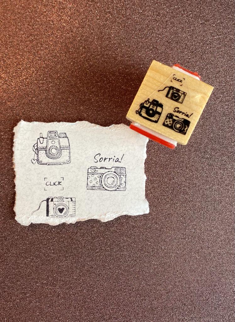 Carimbo de madeira com desenhos de câmaras fotográficas e palavras 'CLICK' e 'Sorria!'
