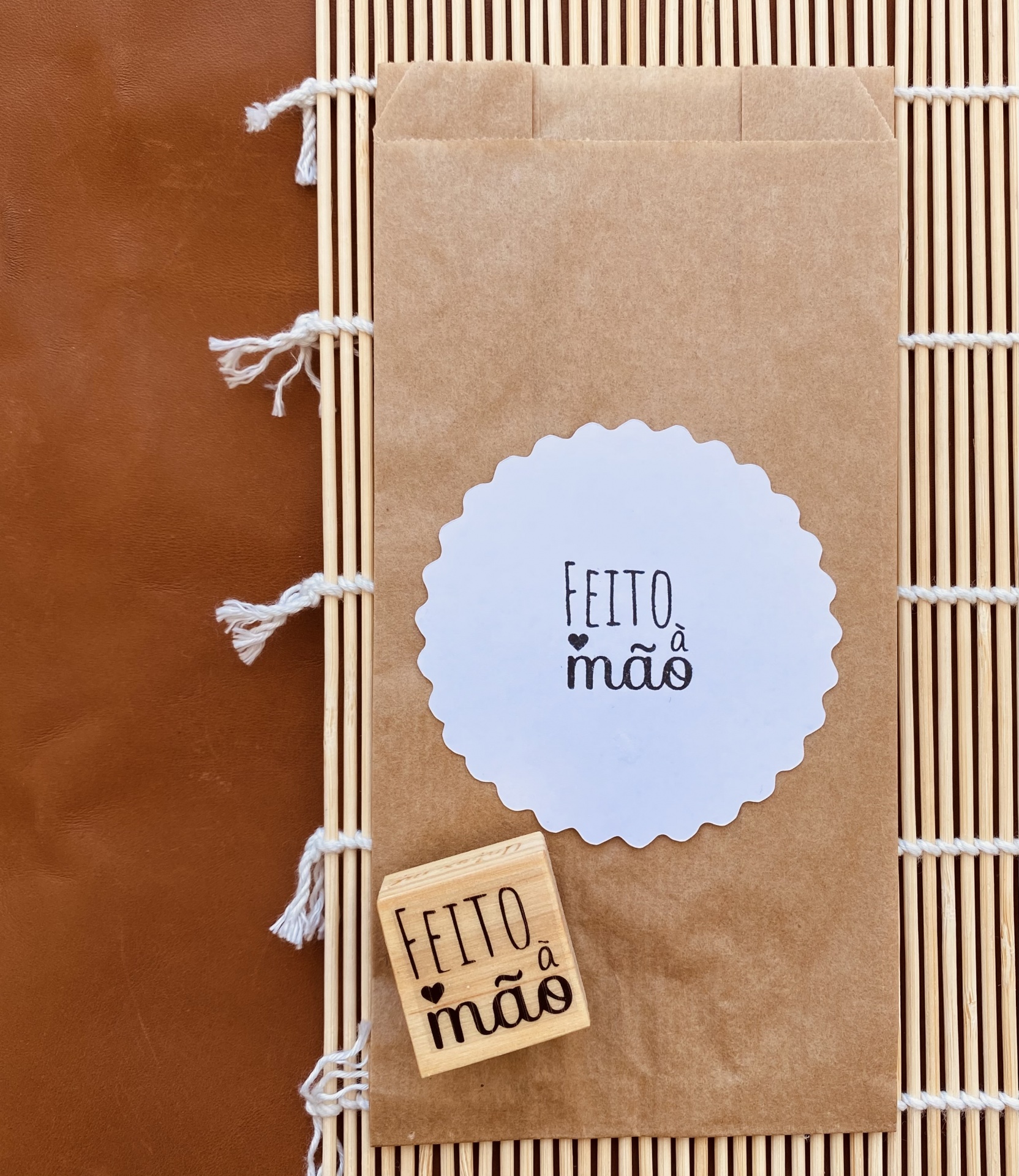 Selo de papel 'FEITO à mão' sobre saco castanho e carimbo de madeira