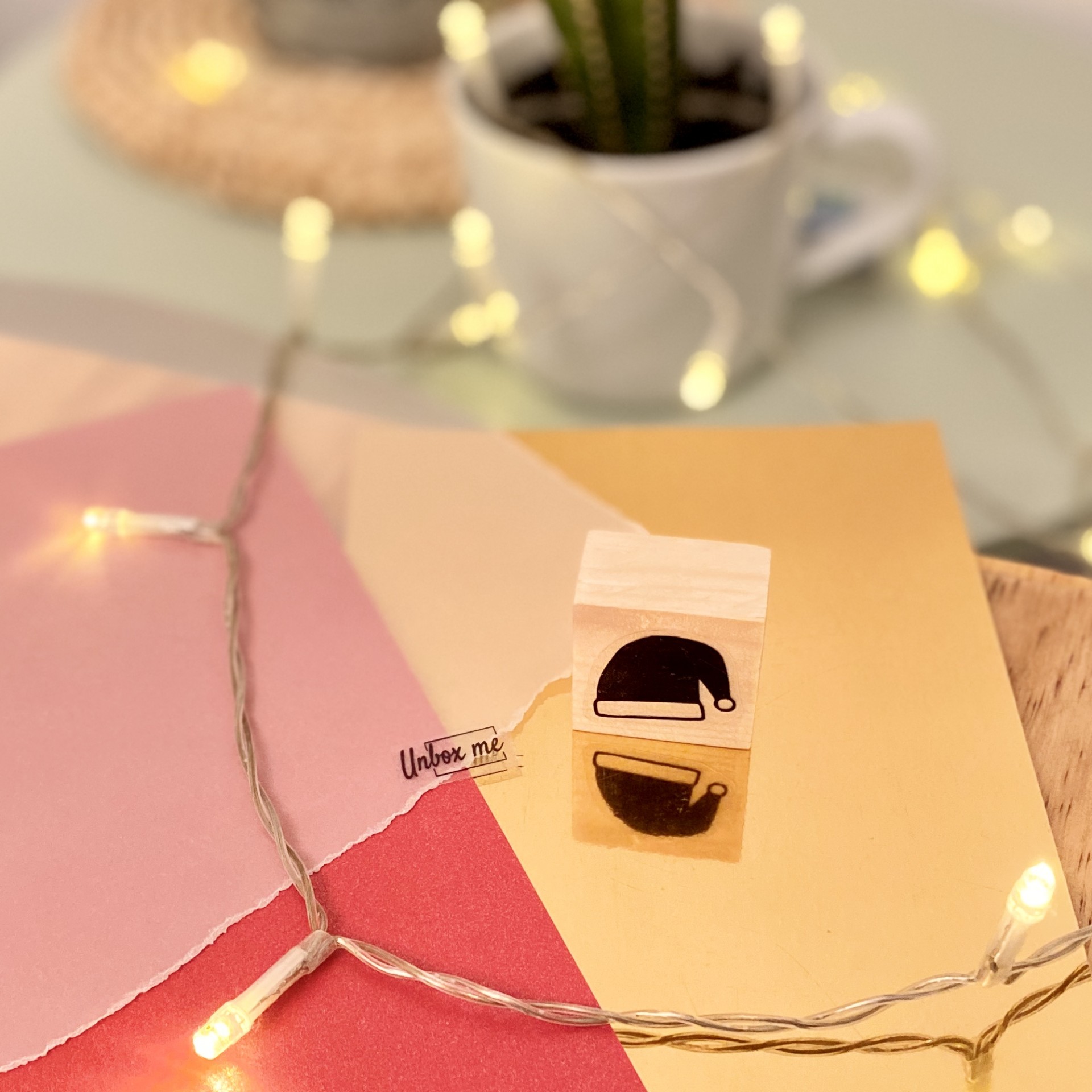 Carimbo de madeira com desenho de caneca e chá sobre papel colorido e luzes decorativas