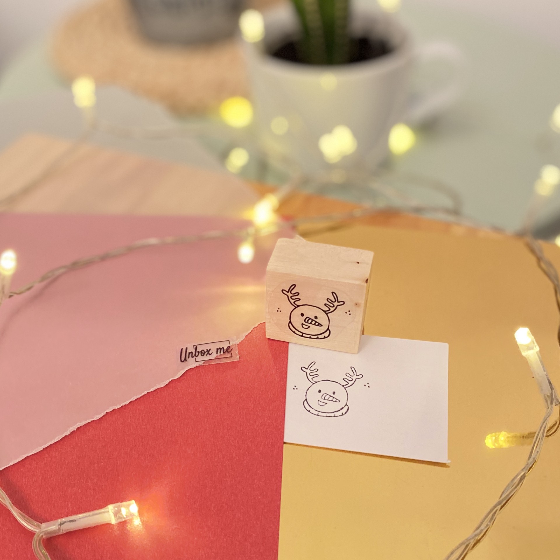 Carimbo de madeira com desenho de alce sorridente num papel branco com luzes decorativas ao redor