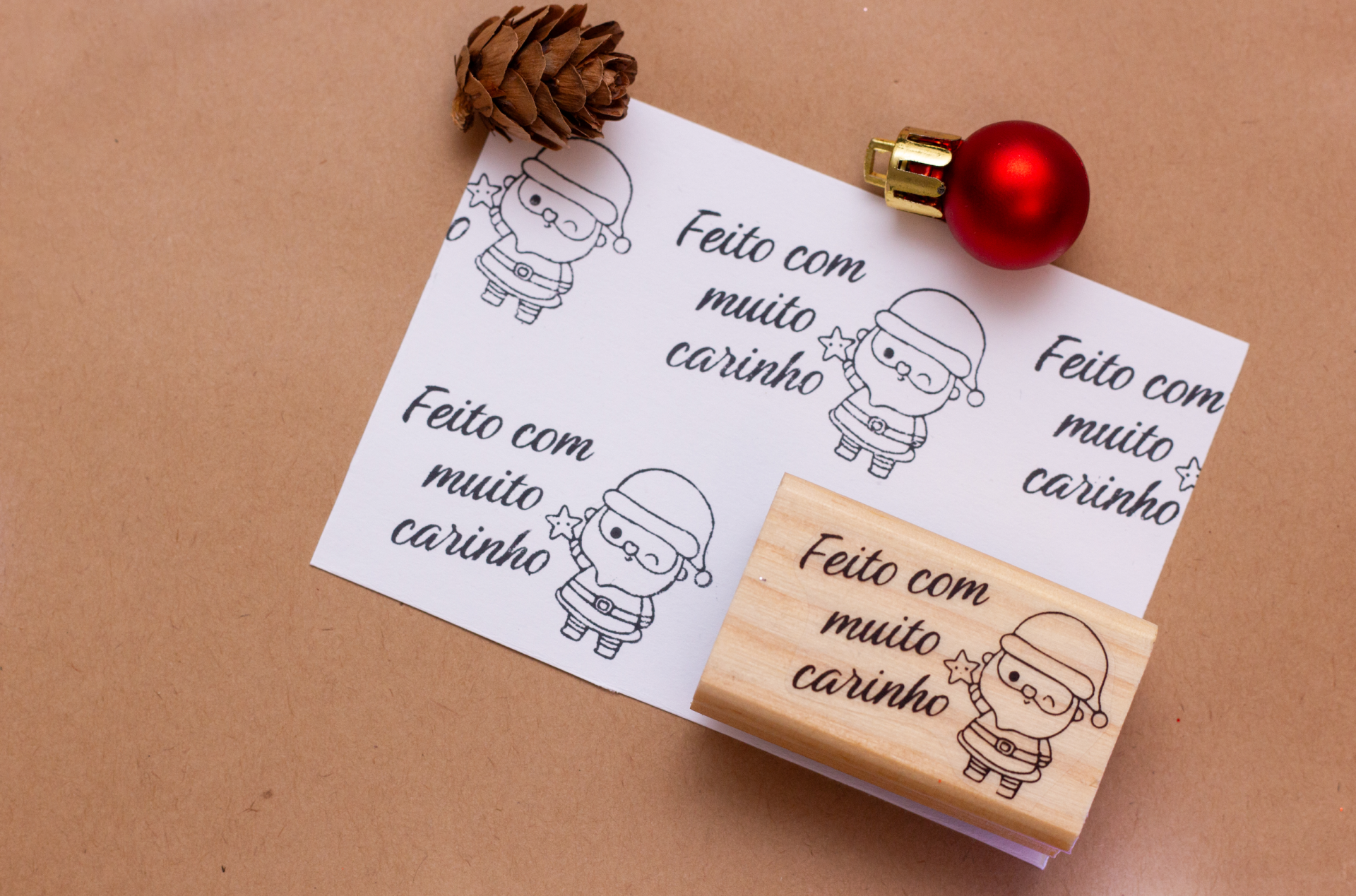 Carimbo de madeira e folha branca com carimbos 'Feito com muito carinho', bola vermelha de Natal e pinheiro