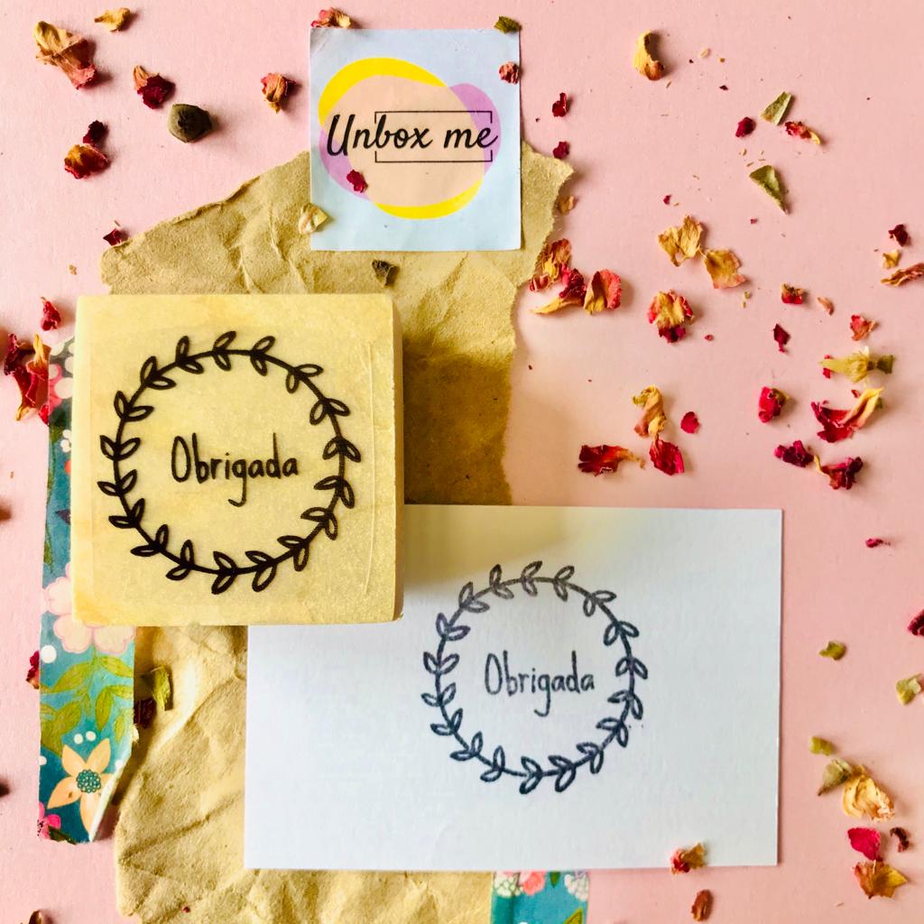 Carimbo de madeira com texto Obrigada, papel impresso e flores secas sobre fundo cor de rosa