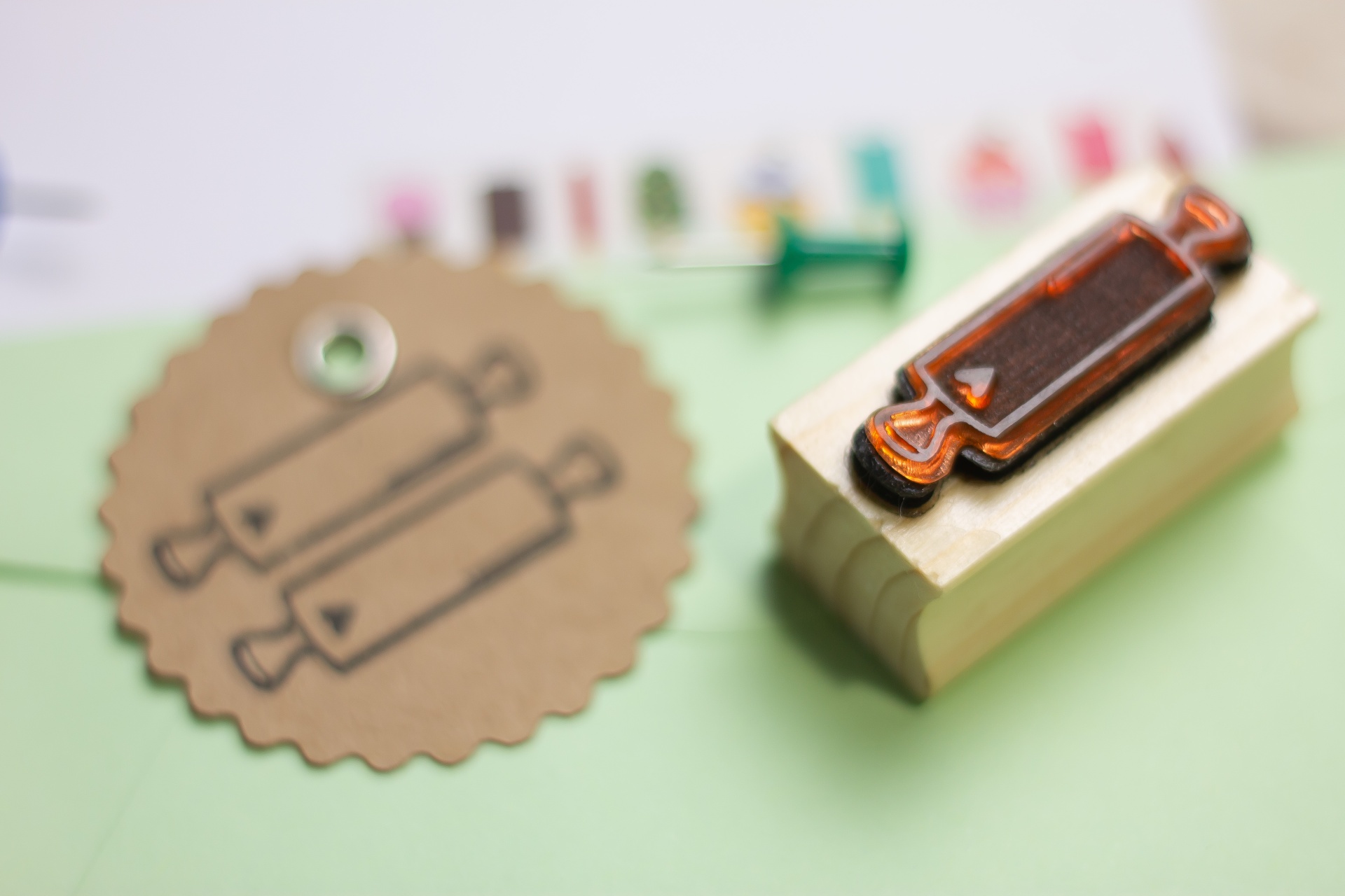 Carimbo de madeira com imagem de pincel e etiqueta castanha correspondente numa mesa verde clara