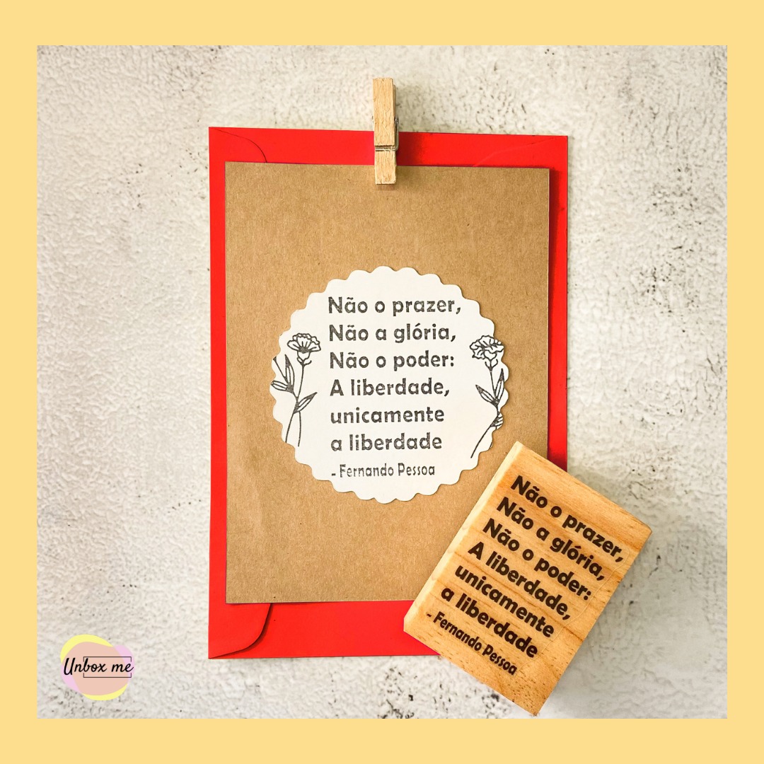 Cartão kraft com citação de Fernando Pessoa e carimbo, envelope vermelho, superfície cinza texturizada.