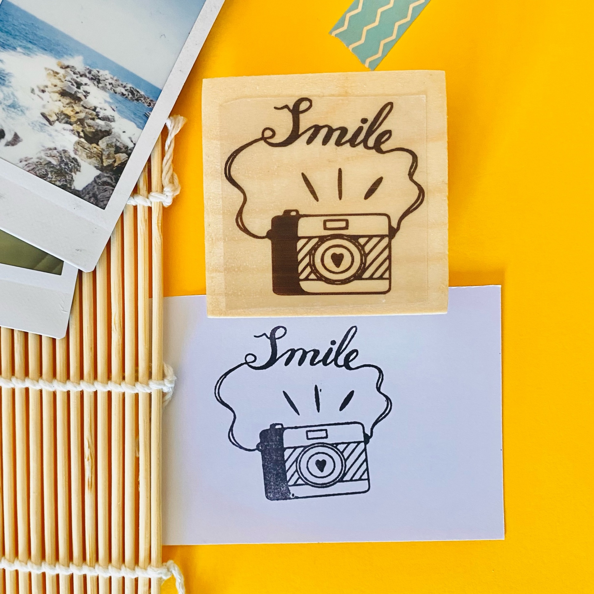 Carimbo de madeira com desenho de câmara e palavra Smile, carimbo impresso em papel branco e elementos decorativos ao fundo