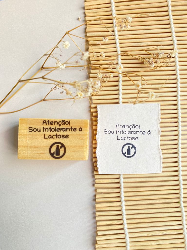 Selo de madeira e impressão em papel com texto sobre intolerância à lactose sobre tapete de bambu e flores secas