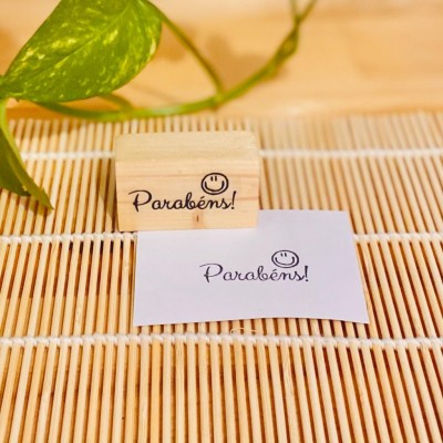 Carimbo de madeira com texto 'Parabéns!' e um sorriso