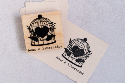 Carimbo de madeira com desenho de gaiola e texto Amar é libertador