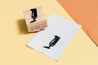 Carimbo de madeira com figura de máquina de barbear preta sobre papel branco rasgado