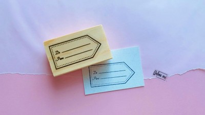 Carimbo de madeira com design de etiqueta e cartão azul carimbado sobre fundo rosa e branco