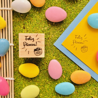 Carimbos de madeira com texto Feliz Páscoa junto a ovos de Páscoa coloridos sobre grama verde.