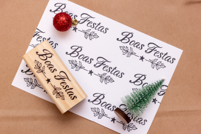 Carimbos de madeira, cartolina com texto 'Boas Festas', árvore e bola de Natal em fundo castanho