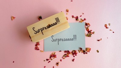 Caixa de madeira pequena com nota cinza e pétalas de flores sobre fundo rosa