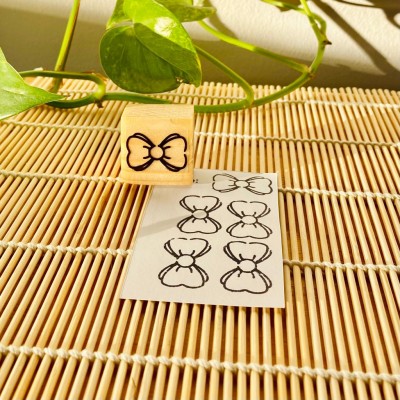 Carimbo de madeira com desenho de laço preto ao lado de papel com carimbos, em superfície de bambu