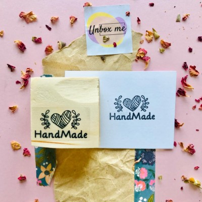 Selo e etiqueta 'HandMade' em papel bege e branco sobre papel kraft, fundo rosa com pétalas secas