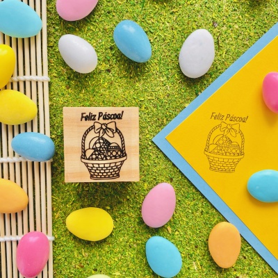 Carimbo de madeira com cesta de Páscoa e ovos coloridos em fundo de relva sintética