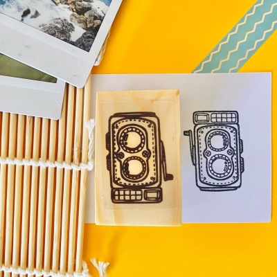 Carimbo de madeira com desenho de câmara fotográfica retro sobre fundo amarelo