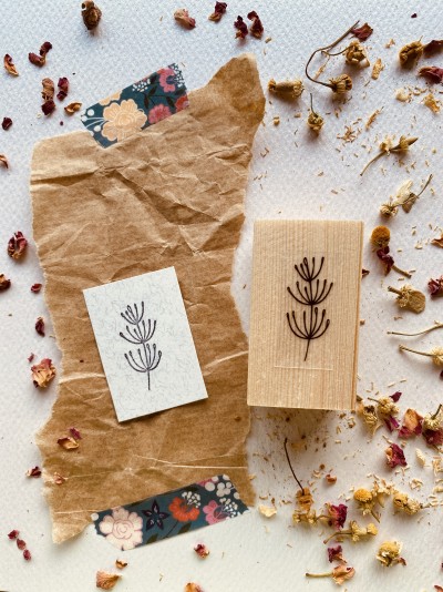 Carimbo de madeira com design floral e papel decorativo em fundo com flores secas