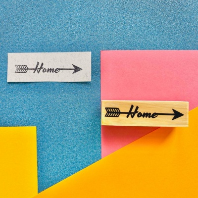 Selo de carimbo de madeira com a palavra Home e seta e carimbo correspondente em papel sobre fundo de cores azul, amarelo, rosa e laranja