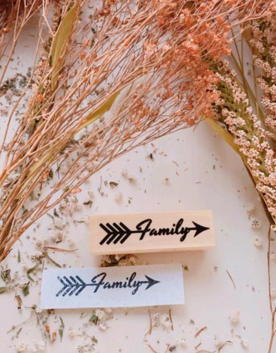Carimbo de borracha com a palavra 'Family' e uma seta preta, com flores secas ao redor