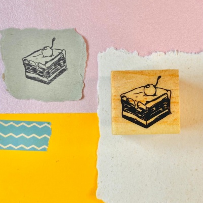 Carimbo de madeira com imagem de fatia de bolo e cereja em papéis coloridos