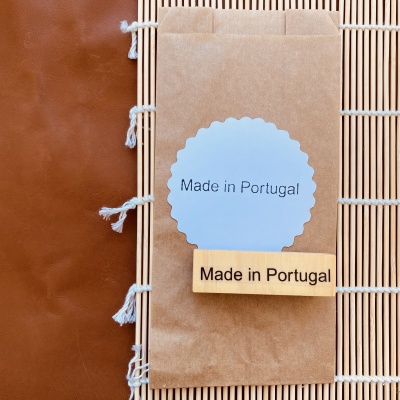 Embalagem de papel castanho com etiqueta azul e carimbo 'Made in Portugal' sobre tapete de palha