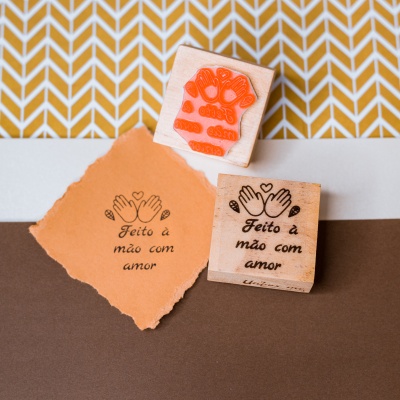 Carimbo de madeira com texto e símbolo de mãos sobre papel e fundo geométrico