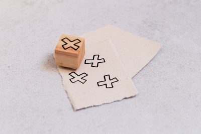 Carimbo de madeira com X preto e papéis com marcas carimbadas.