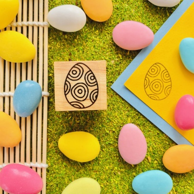 Selo de madeira com padrão em ovo decorativo e ovos de páscoa coloridos sobre fundo verde