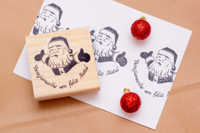 Carimbo de madeira com desenho de Pai Natal e texto de Natal, papel impresso e bolas de Natal vermelhas