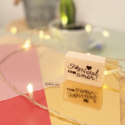 Carimbo de madeira com frase de Natal em superfície espelhada dourada e luzes decorativas