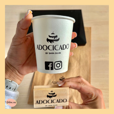 Copo de papel branco com logotipo ADOCICADO, carimbo de madeira e saco ao fundo