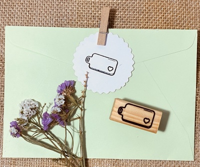 Envelope verde com papel redondo branco e carimbos de etiquetas com coração, flores secas ao lado