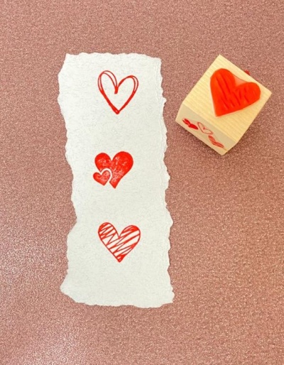 Carimbo de madeira com coração vermelho e impressões em papel branco sobre fundo rosa