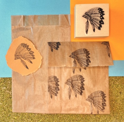 Selo de madeira com imagem de cocar indígena e embalagens de papel carimbadas com o mesmo desenho